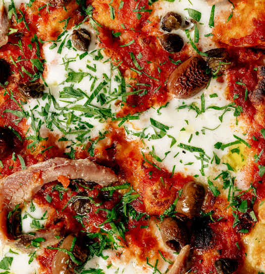 Close-up of a pizza topped with mushrooms, olives, and fresh herbs.