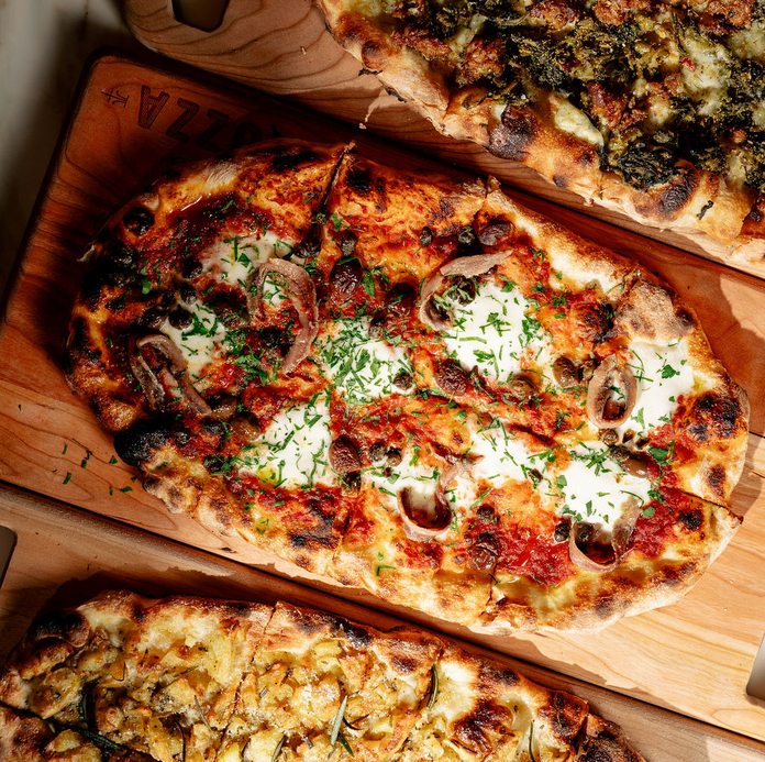 Three artisan pizzas on wooden boards, topped with various ingredients like mushrooms, herbs, and cheese.
