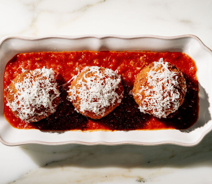 Three meatballs with white cheese topping in red sauce on a white dish.