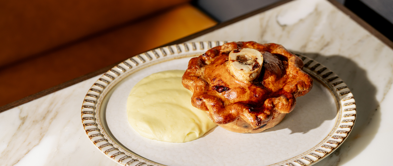 A flaky pastry with a creamy filling sits on a white plate with a marble tray.